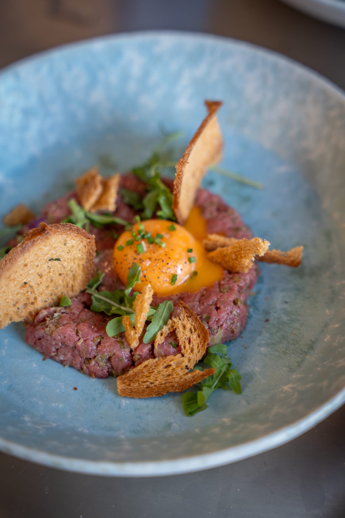 Steak tartare met eidooier, toast en rucola in een blauwe kom